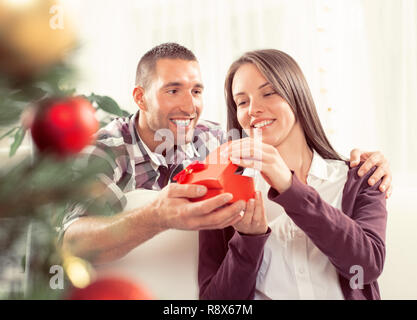 Jeune homme donne à sa petite amie un cadeau de Noël. Elle est heureuse pendant l'ouverture de boîte-cadeau. Banque D'Images