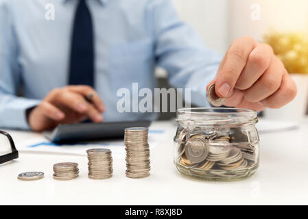 L'homme calcule les économies. Concept de planification budgétaire. Businessman travaillant dans le bureau. Homme met des pièces dans le jar Banque D'Images