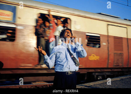 Man talking on mobile phone in front of running train local à Bombay Mumbai en Inde. Communiqué de modèle numéro 202 Banque D'Images