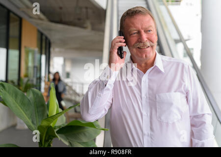 Happy senior businessman thinking tout en parlant au téléphone dans la ville Banque D'Images