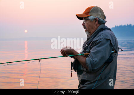 Caucasian man lier une mouche sur sa ligne alors que la pêche à la mouche La pêche au saumon et à la truite fardée searun à Puget Soud près de Port Orchard, Washington USA. Banque D'Images