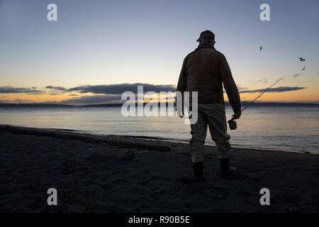 Un pêcheur de mouche s'apprête à jeter dans l'eau salée au lever du soleil et pêcher à la mouche pour le saumon et la truite fardée côtière sur une plage au nord ouest coastli Banque D'Images