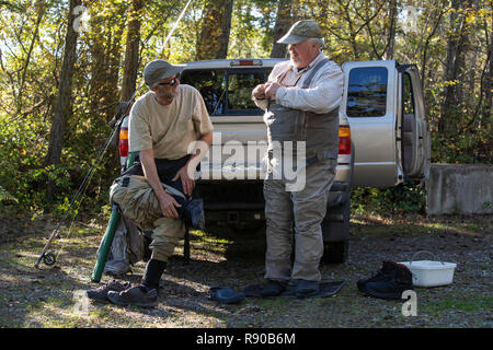 Homme de race blanche deux pêcheurs à la mouche profitez d'une conversation autour d'une camionnette tout en mettant sur leurs échassiers d'aller pêcher à la mouche. Banque D'Images