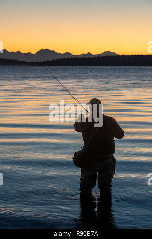 Un pêcheur de mouche s'apprête à jeter dans l'eau salée au lever du soleil et pêcher à la mouche pour le saumon et la truite fardée côtière sur une plage au nord ouest coastli Banque D'Images