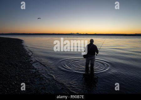 Un pêcheur de mouche s'apprête à jeter dans l'eau salée au lever du soleil et pêcher à la mouche pour le saumon et la truite fardée côtière sur une plage au nord ouest coastli Banque D'Images