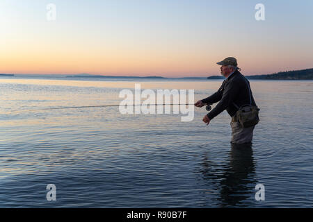 Une vue latérale d'un pêcheur de mouche au lever du soleil pour le saumon et la truite fardée côtière searun à partir d'une plage d'eau salée sur une plage au nord ouest c Banque D'Images