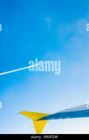 Vue partielle de l'aile d'un avion à une certaine distance un autre avion avec traînée de condensation contre le ciel bleu Banque D'Images
