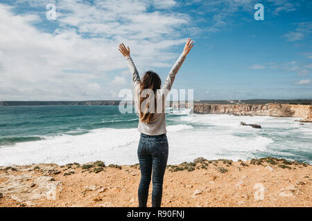 Vue arrière d'une jeune fille d'admirer la vue magnifique sur l'océan Atlantique et le paysage et élever ses mains en montrant comment elle aime et le plaisir qu'elle est. Banque D'Images