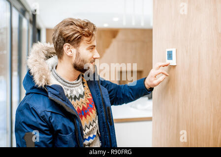 L'homme dans des vêtements d'hiver froid réglage de la température avec thermostat électronique à la maison Banque D'Images