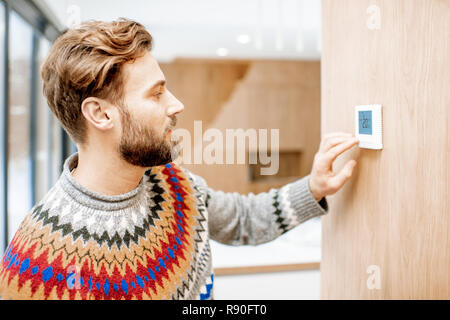 Pull homme dans une sensation de froid réglage de la température avec thermostat électronique à la maison Banque D'Images