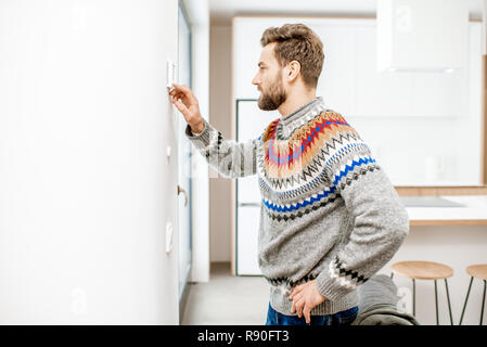 Pull homme en ajustant la température avec thermostat électronique à la maison Banque D'Images