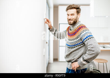 Pull homme en ajustant la température avec thermostat électronique à la maison Banque D'Images