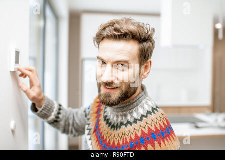 Portrait d'un homme dans la salle de réglage pull avec thermostat électronique de température à la maison Banque D'Images