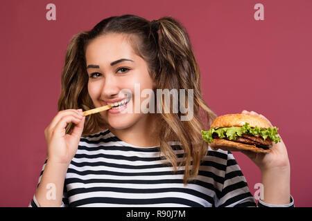 Femme manger burger. Close up face portrait fille avec restauration rapide sur fond rose coloré Banque D'Images