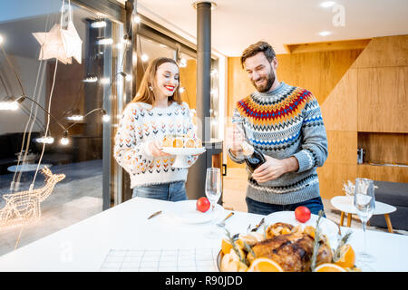 Jeune couple ayant dîner de fête assis ensemble dans la maison moderne durant les vacances d'hiver Banque D'Images