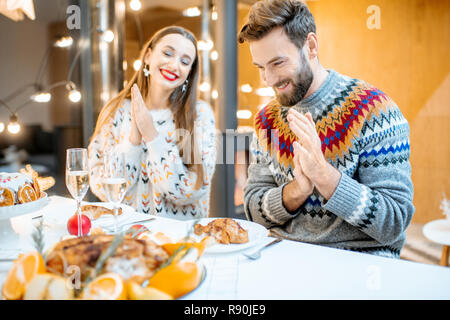 Jeune couple ayant dîner de fête assis ensemble dans la maison moderne durant les vacances d'hiver Banque D'Images