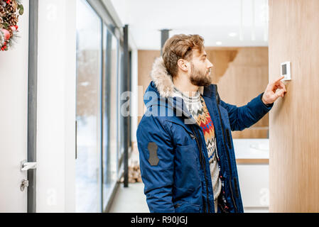 L'homme dans des vêtements d'hiver froid réglage de la température avec thermostat électronique à la maison Banque D'Images