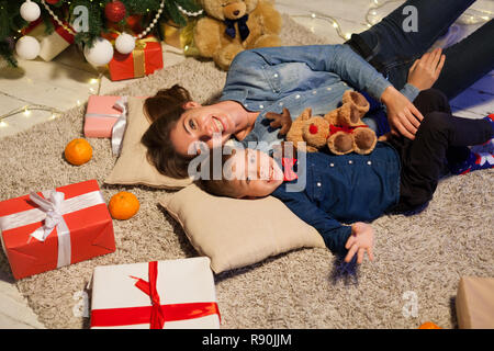 Maman avec fils gisant sur le sol à proximité d'un arbre de Noël avec des cadeaux Banque D'Images