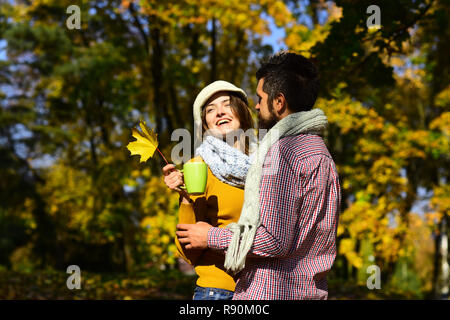 Le romantisme et l'humeur d'automne concept. Couple in love avec la feuille jaune et foulards détient tasse à café. Fille et barbu ou en amoureux sur une date hug. L'homme et de la femme avec des visages souriants sur les arbres d'automne background Banque D'Images