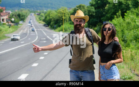 Voiture voyageurs essayent d'arrêter. L'auto-stop est l'un des moyens les moins coûteux de voyager. Auto-stoppeurs couple voyageant de l'été journée ensoleillée. Voyageurs Couple man and girl l'auto-stop au bord de la route fond nature. Banque D'Images