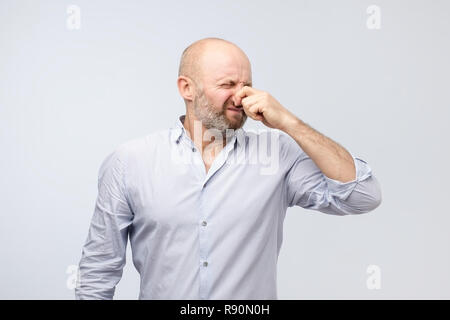 Odeur fétide mature man in shirt holding nez Banque D'Images