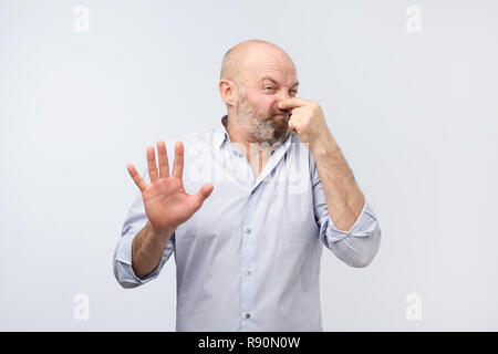 Odeur fétide mature man in shirt holding nez Banque D'Images