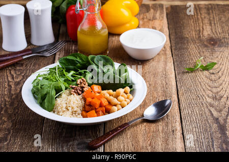 Bol à salade saine avec des citrouilles, pois chiches, quinoa, roquette, noix et vinaigrette au yogourt sur table en bois rustique, selective focus Banque D'Images