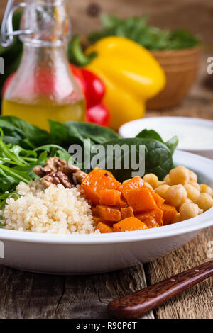 Bol à salade saine avec des citrouilles, pois chiches, quinoa, roquette, noix et vinaigrette au yogourt sur table en bois rustique, selective focus Banque D'Images