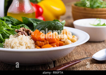 Bol à salade saine avec des citrouilles, pois chiches, quinoa, roquette, noix et vinaigrette au yogourt sur table en bois rustique, selective focus Banque D'Images