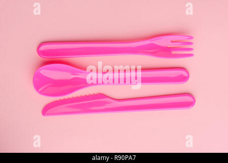 Couverts en plastique lumineux situé sur fond rose. Couteau mignon, cuillère et fourchette pour les jeux des enfants. Banque D'Images