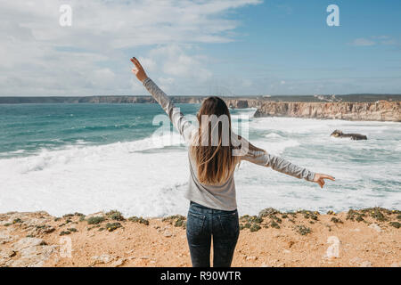 Vue arrière d'une jeune fille d'admirer la vue magnifique sur l'océan Atlantique et le paysage et élever ses mains en montrant comment elle aime et le plaisir qu'elle est. Banque D'Images