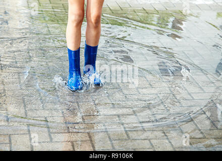 Fille en bleu bottes de caoutchouc debout dans une flaque d'eau après une pluie outdoor le jour d'été. jambes libre Banque D'Images