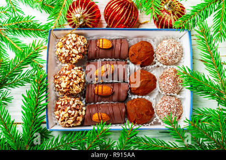 Ensemble de chocolats. Truffes aux amandes, noix de coco et de cookie dans une boîte sur un vieux tableau blanc avec des branches de sapin. Cadeau pour Noël et Nouvel an. Banque D'Images