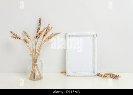 Maquette du châssis vertical avec seigle sauvage bouquet en vase en verre près de mur blanc. Cadre vide maquette pour sa présentation. Pour l'ossature du modèle ar moderne Banque D'Images