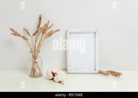 Maquette du châssis vertical avec seigle sauvage bouquet en vase en verre près de mur blanc. Cadre vide maquette pour sa présentation. Pour l'ossature du modèle ar moderne Banque D'Images