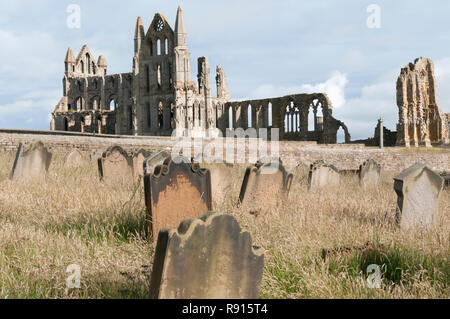 Il ruines de l'abbaye de Whitby vu à travers les pierres tombales dans le cimetière de l'église St Mary. Banque D'Images