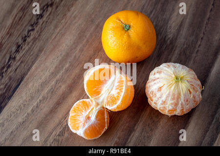 Trois oranges de satsuma sur une table en bois rustique, deux oranges pelées, l'un en suprêmes Banque D'Images