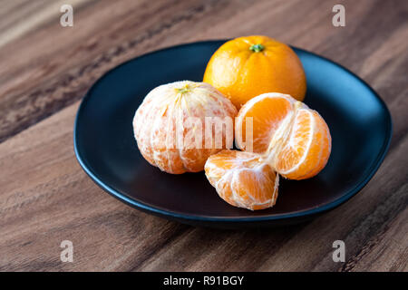 La plaque noire de satsuma oranges sur une table en bois rustique, deux oranges pelées, l'un en suprêmes Banque D'Images