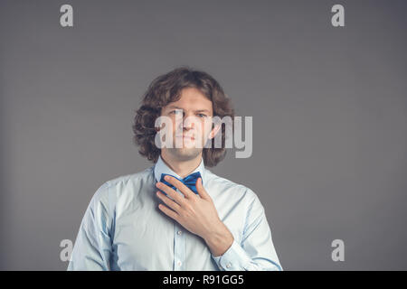 Portrait de jeune homme hipster adapter son miroir dans Bow tie isolé sur fond gris. Cheveux bouclés sombres groom en chemise bleue la préparation de meeti Banque D'Images