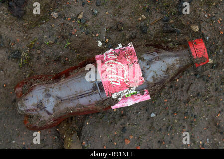 Une sale les plastiques de bouteille de Coca Cola dans la boue à l'ancien site de l'usine IBM dans Spango Valley, Greenock, Scotland Banque D'Images