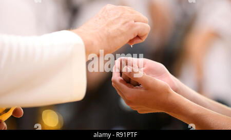 Close up image d'un paroissiens les mains jointes recevant le pain au cours de la sainte communion d'un prêtre catholique à la messe. Banque D'Images