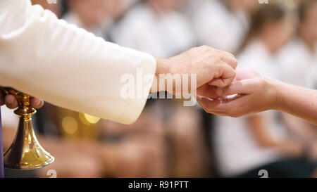 Close up image d'un paroissiens les mains jointes recevant le pain au cours de la sainte communion d'un prêtre catholique à la messe. Banque D'Images