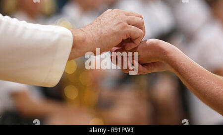 Close up image d'un paroissiens les mains jointes recevant le pain au cours de la sainte communion d'un prêtre catholique à la messe. Banque D'Images