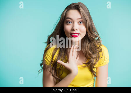 Surpris jeune femme sur fond bleu. Looking at camera sous le choc et avec le sourire. Une jeune fille demande qui je suis, montrant sur eux-mêmes les doigts. Positif Banque D'Images