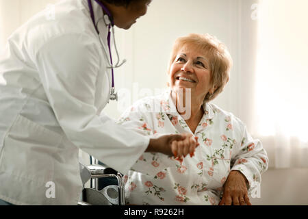 Heureux femme âgée étant assisté par une femme médecin tout en restant assis dans un fauteuil roulant. Banque D'Images