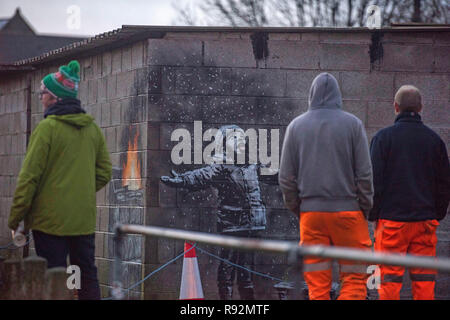 Port Talbot, Pays de Galles, Royaume-Uni. 19 Décembre, 2018. Les résidants locaux de Taibach à Port Talbot inspecter que graffiti est apparu du jour au lendemain sur un garage qui est par l'artiste de rue anonyme Banksy. L'illustration montre un enfant à bras ouverts à l'affiche dans ce qui semble être la neige avec une luge à côté de lui, mais l'autre côté du mur révèle c'est ash à partir d'une poubelle en feu. Credit : Phil Rees/Alamy Live News Banque D'Images