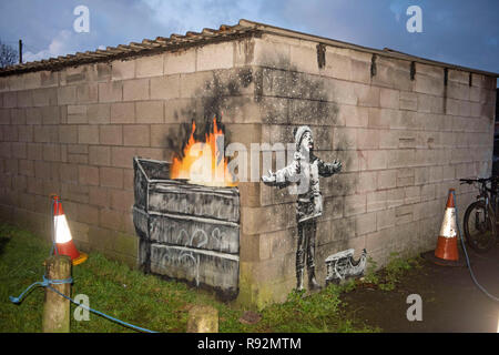 Port Talbot, Pays de Galles, Royaume-Uni. 19 Décembre, 2018. Le graffiti qui est apparu sur un garage dans la région de Port Talbot Taibach qui est répandu pour être par l'artiste de rue anonyme Banksy. Les fêtes de fin d'artwork montre un enfant à bras ouverts à l'affiche dans ce qui semble être la neige avec une luge à côté de lui, mais l'autre côté du mur révèle c'est ash à partir d'une poubelle en feu. Credit : Phil Rees/Alamy Live News Banque D'Images