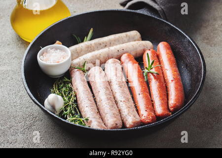 Les saucisses crues frais avec le thym, le romarin et l'ail dans une poêle en fonte sur une table en béton. Banque D'Images