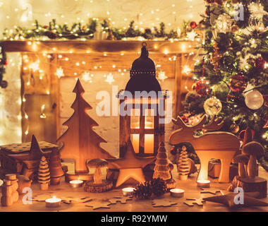 Les jouets en bois, les figures, les étoiles, l'orignal, l'arbre de la fourrure lanterne sur table en face d'une cheminée, décorées mantel, arbre de Noël avec des ornements de Noël, des guirlandes, des lumières des bougies, selective focus, tonique Banque D'Images