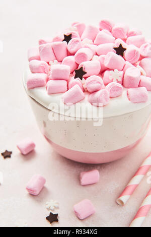 Chocolat chaud ou de cacao avec crème fouettée et bonbons rose en rose et blanc rayé rose tasse avec paille sur fond rose abstrait. Top v Banque D'Images